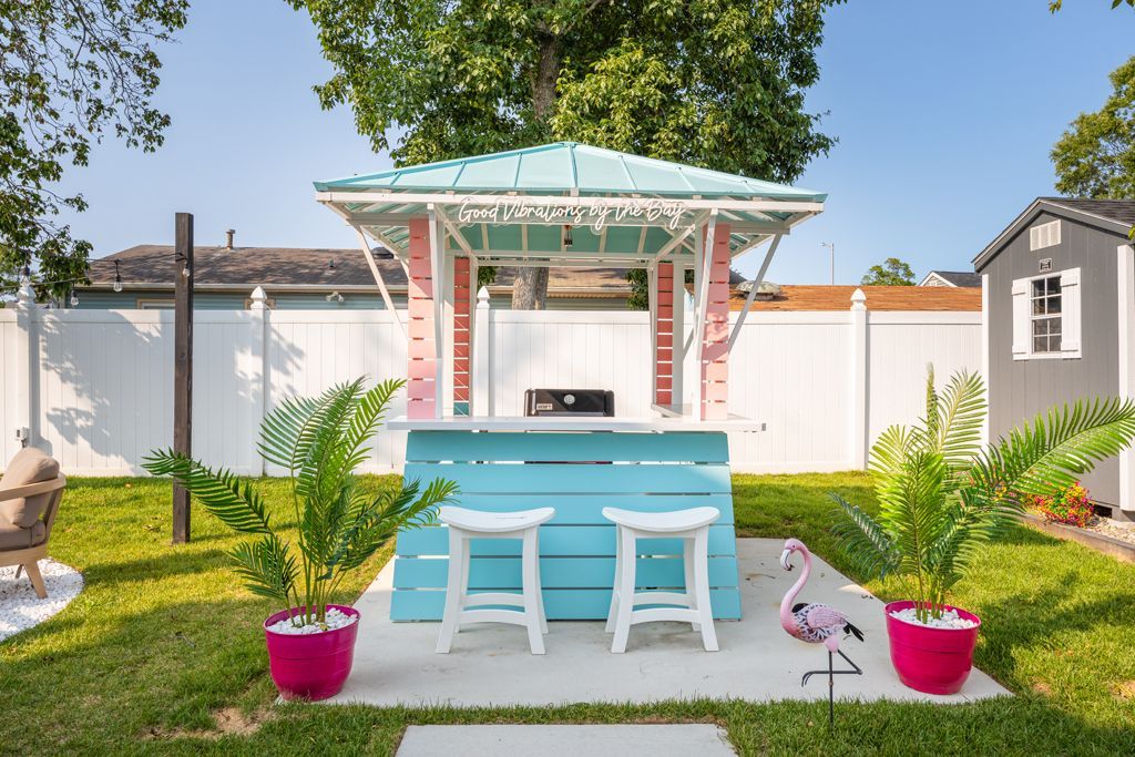 Backyard bar with teal and pink accents, two stools, and a flamingo statue.