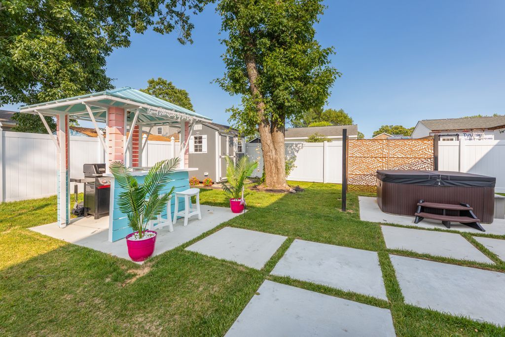 Backyard patio with bar, grill, hot tub, and concrete squares on the lawn.