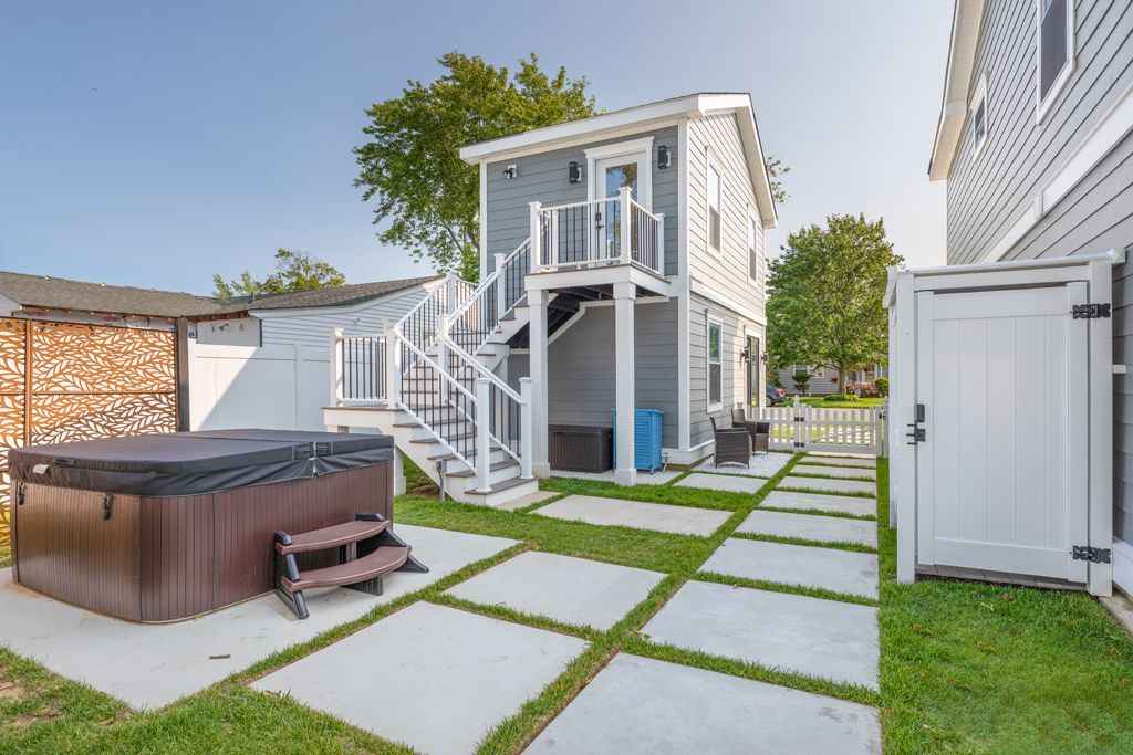 Backyard with hot tub, two-story structure with outdoor stairs, concrete pavers, and green lawn.