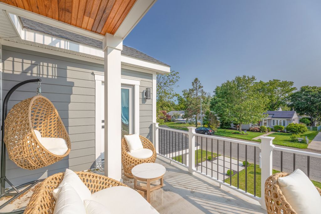 Balcony with wicker furniture, hanging chair, and view of houses and trees on a sunny day.