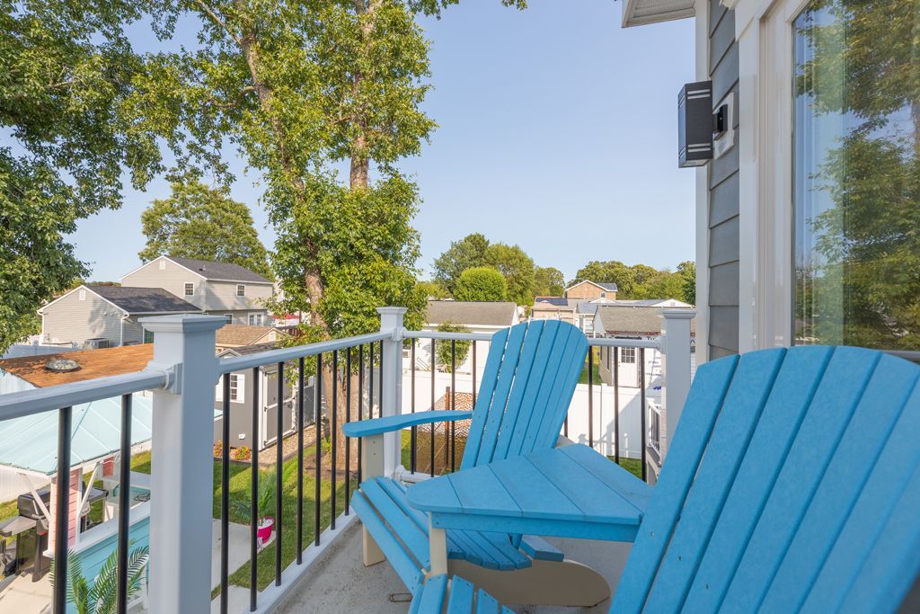 Two blue Adirondack chairs on a balcony overlooking a neighborhood with green trees and houses.