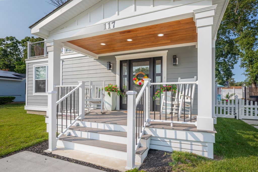 Small house with a covered porch. White trim, gray siding, black door, and a wooden porch ceiling.