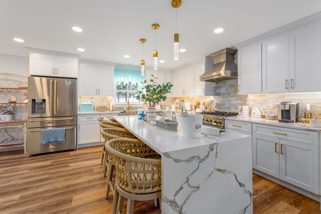 Bright, white kitchen with a large island, gold accents, and a stainless steel refrigerator.