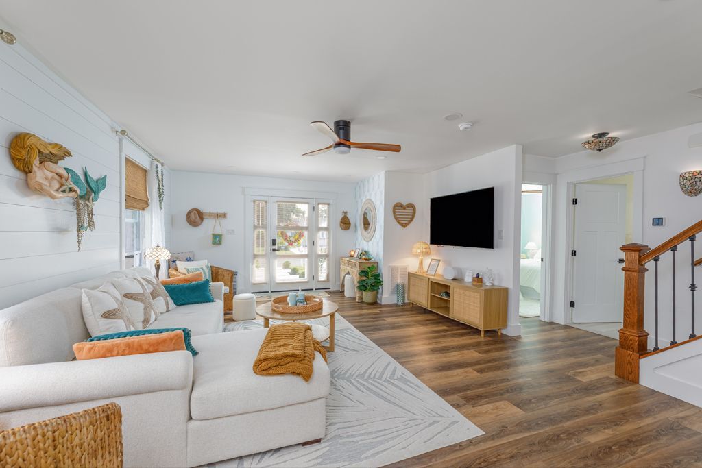 Cozy living room with white sectional, light wood floors, TV, and beachy decor.