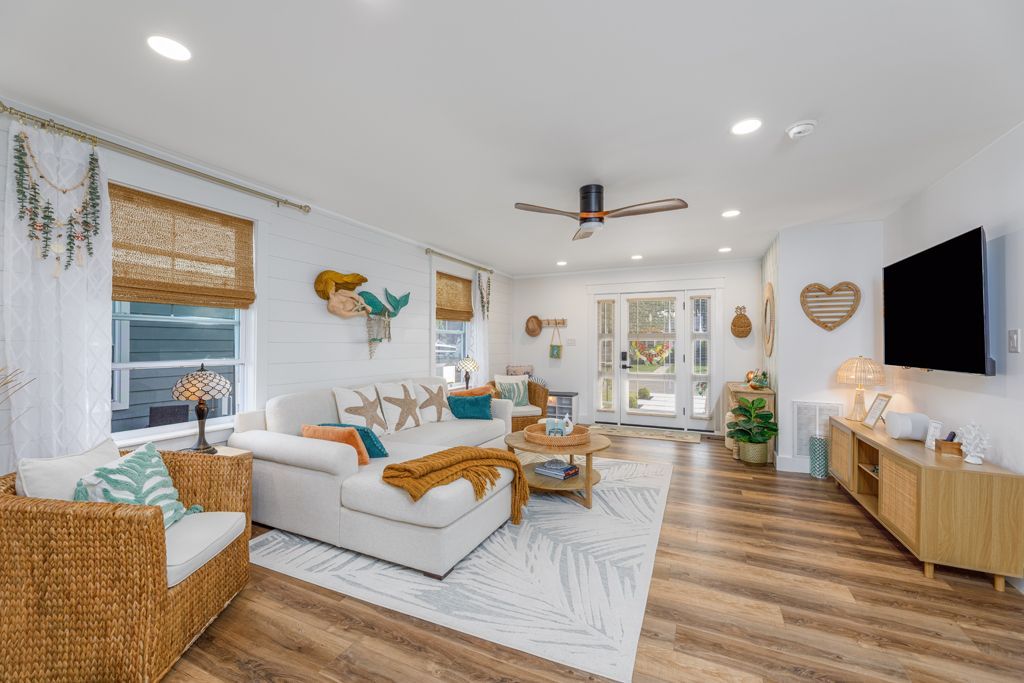 Living room with white sofa, rattan chair, wooden floors, coastal decor, and a television.