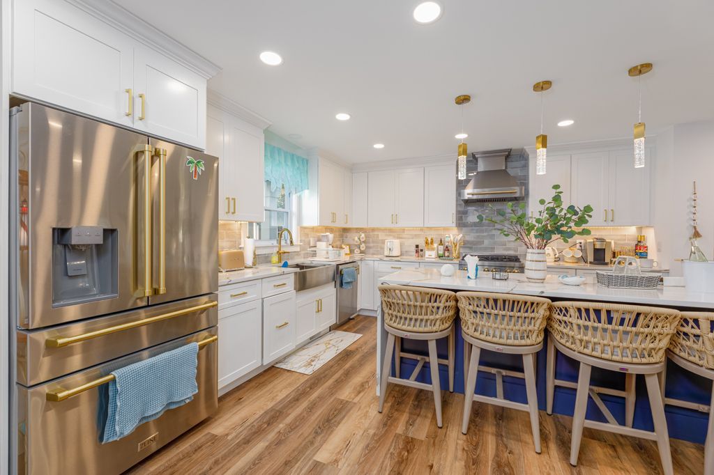 Bright kitchen with stainless steel refrigerator, white cabinets, island with blue base, and wood flooring.