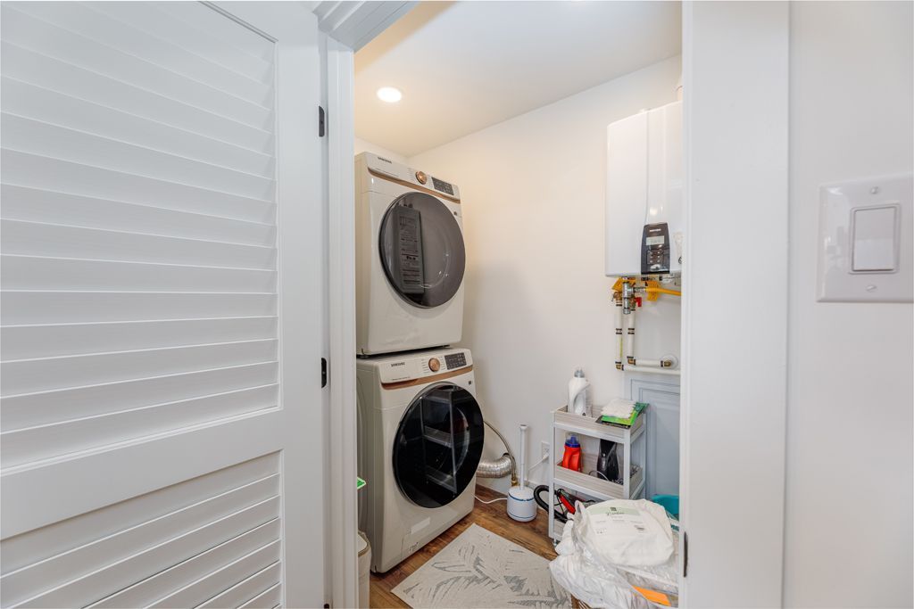 Small laundry room with stacked washer and dryer, white cabinets, and open door.