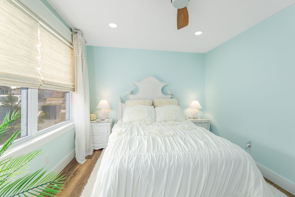 Bedroom with light blue walls, white bed, nightstands, and window with blinds.