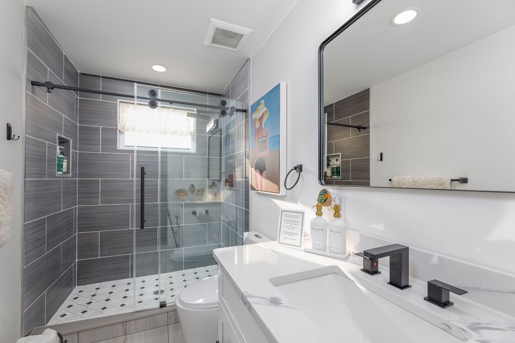 Modern bathroom with white and gray tiling, glass shower, black fixtures, and a large mirror.