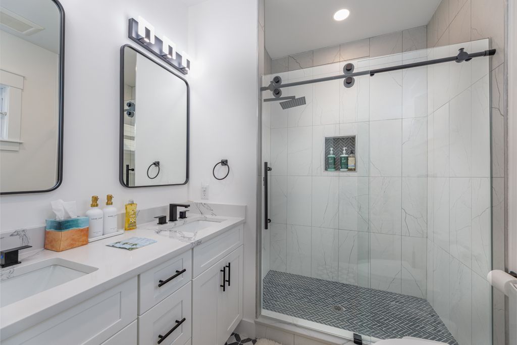 Modern white bathroom with double sinks, a glass shower, and black accents.