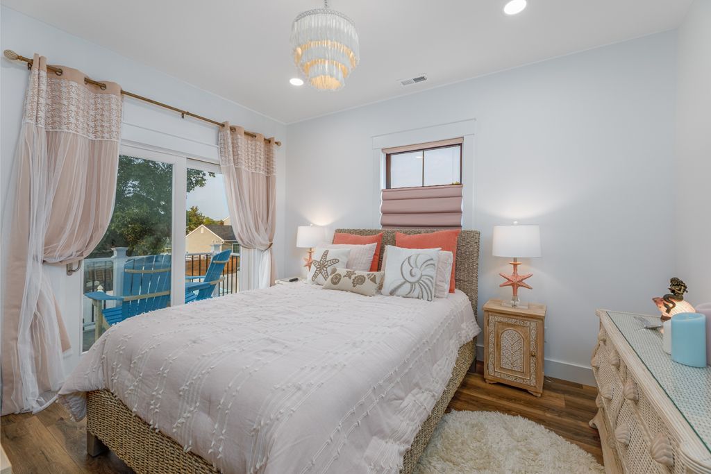 Bedroom with a bed, nightstand, and sliding glass door with sheer curtains; light colors.