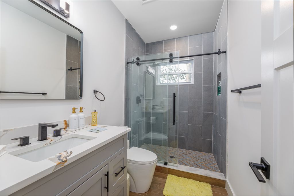 Modern bathroom with gray tile shower, white vanity, and black hardware.