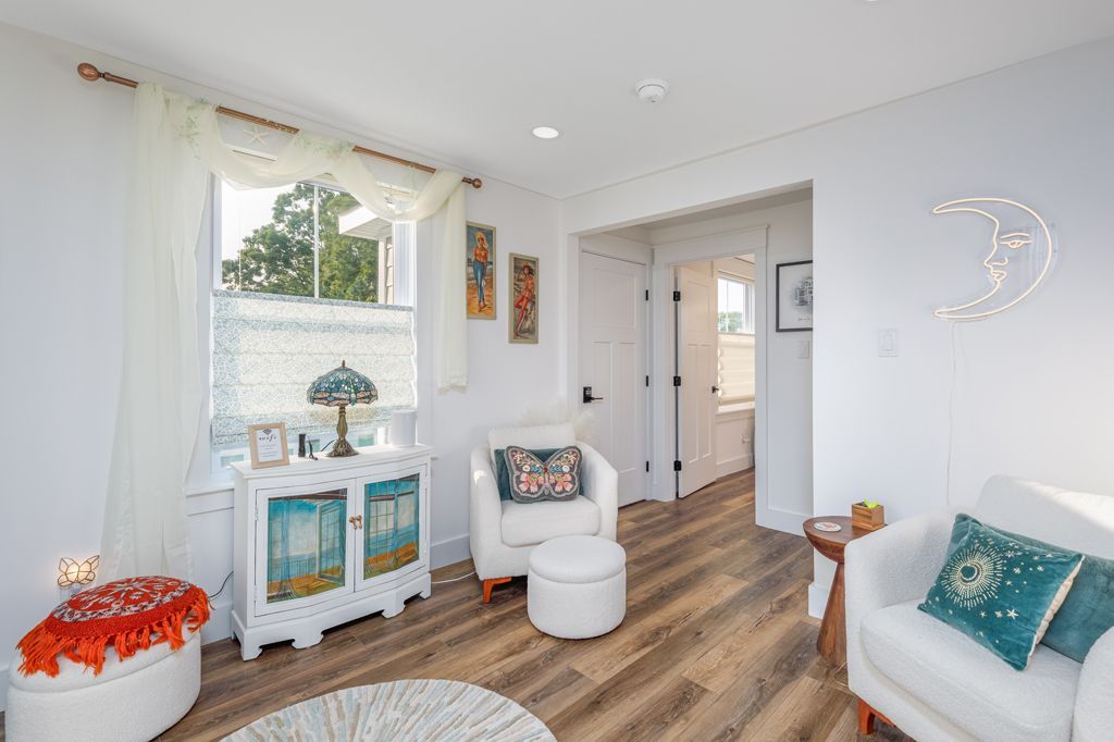 Cozy white living room with wood floors, two armchairs, a cabinet, and a window. A decorative moon hangs on the wall.