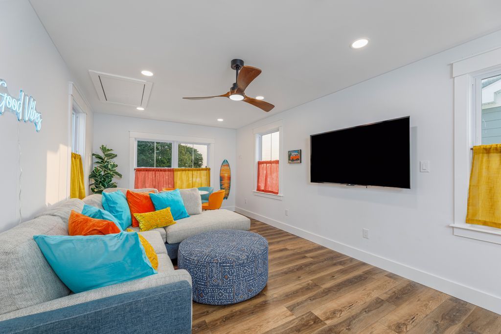 A brightly colored living room with a sectional sofa, TV, and patterned ottoman.