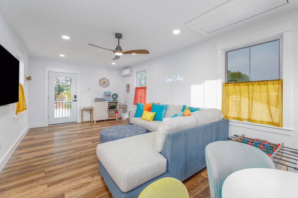 A bright living room with a blue sectional, yellow curtains, and light wood flooring.