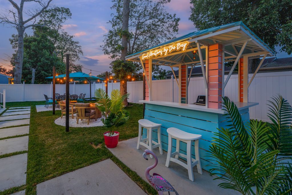 Backyard bar with teal and pink accents, white stools, and a pink flamingo. Evening sky.