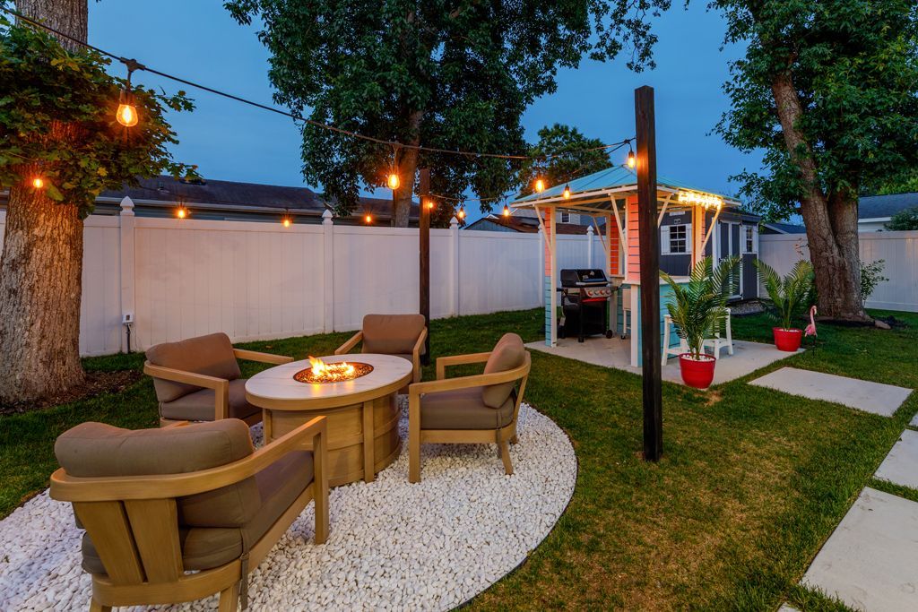 Backyard patio with fire pit, seating, string lights, and small tiki bar.
