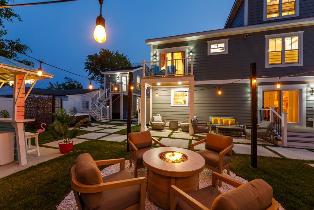 Backyard patio at dusk with fire pit, seating, string lights, and a house.