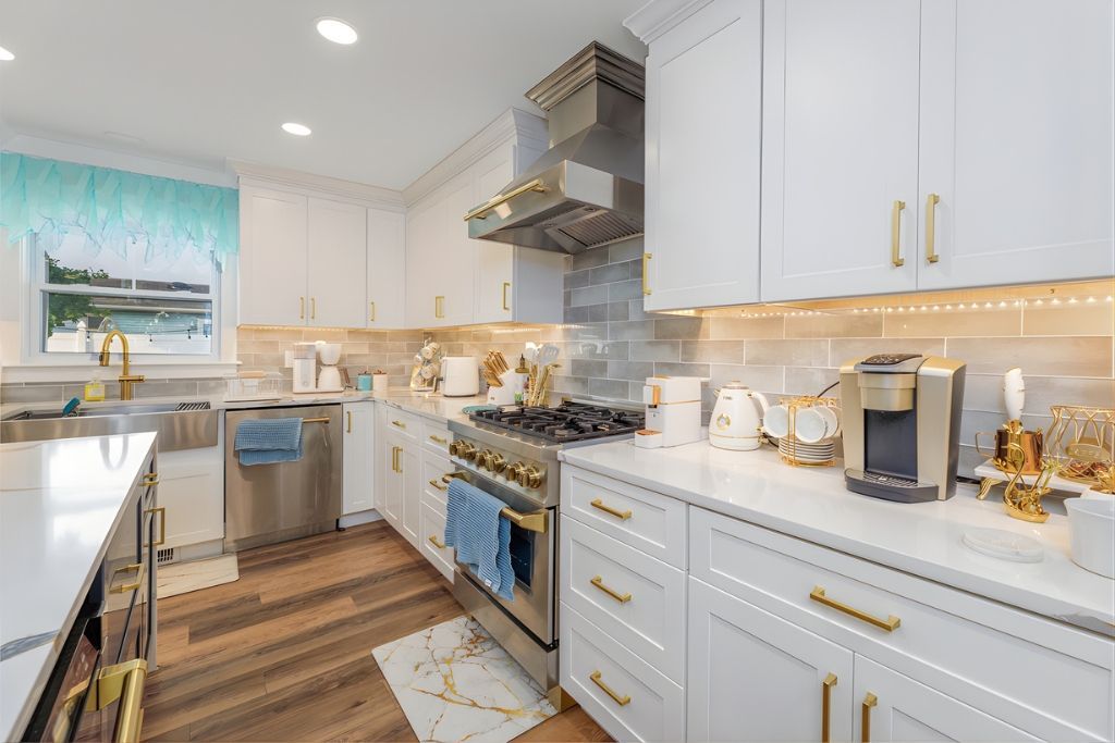 Bright, white kitchen with gold hardware. Stainless steel appliances and light brown wood floors.