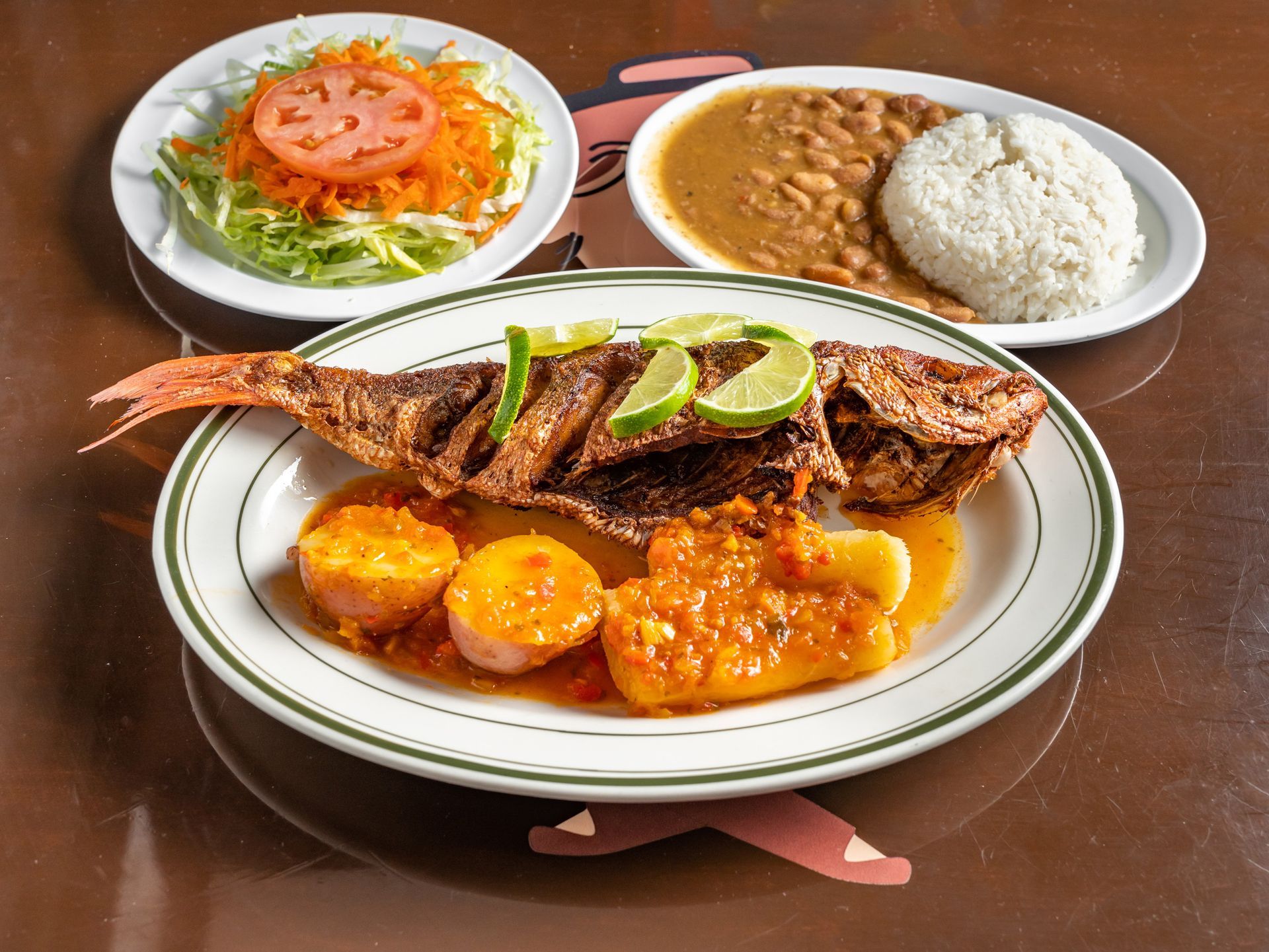 A plate of Colombian food with a fish , potatoes , beans and rice on a table.
