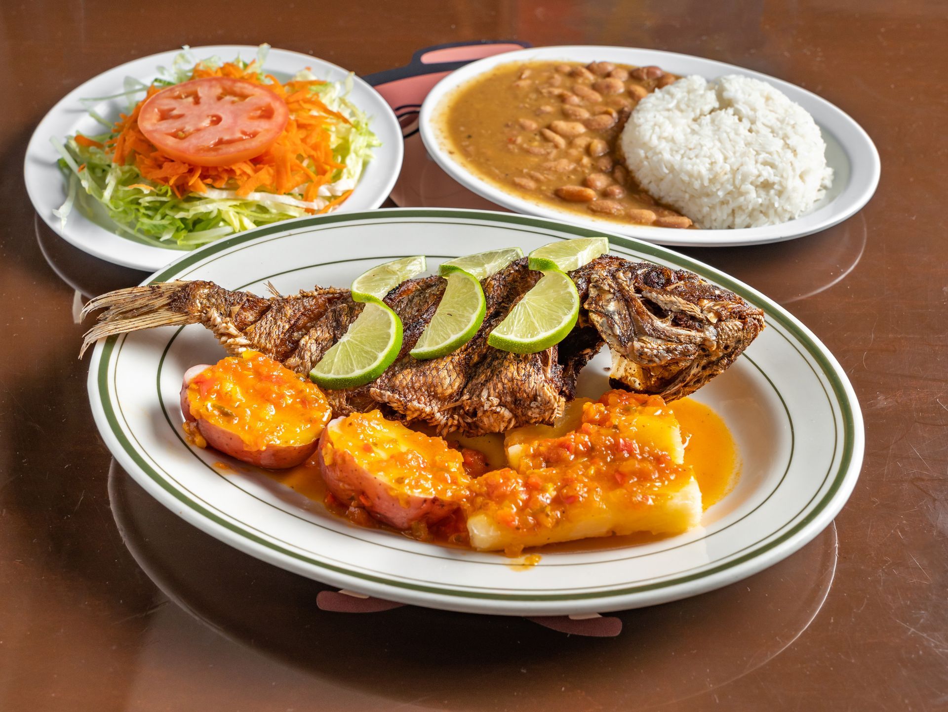 A plate of Colombian food with a fish , potatoes , rice and beans on a table.