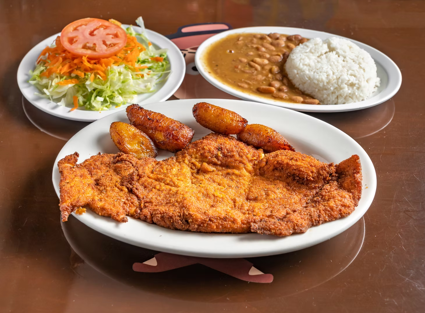 A plate of Colombian  food with rice , beans , and a salad on a table.
