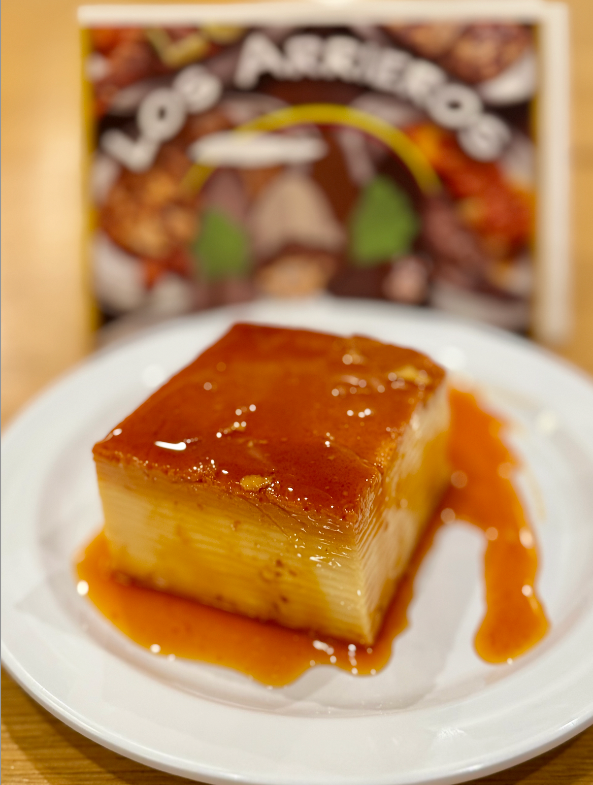 A white plate topped with a piece of flan dessert with sauce on it.