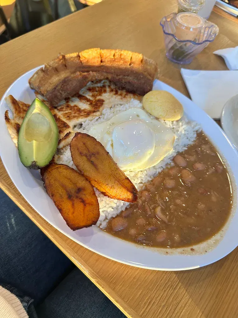 A white plate topped with rice , beans , eggs , and avocado on a wooden table.