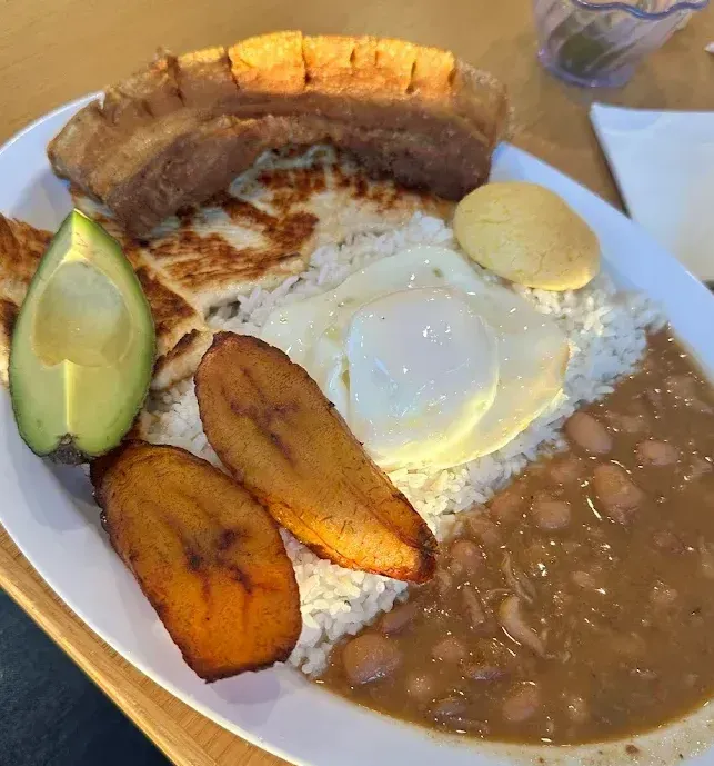 A plate of Colombian food with rice , beans , eggs , bananas and avocado on a table.