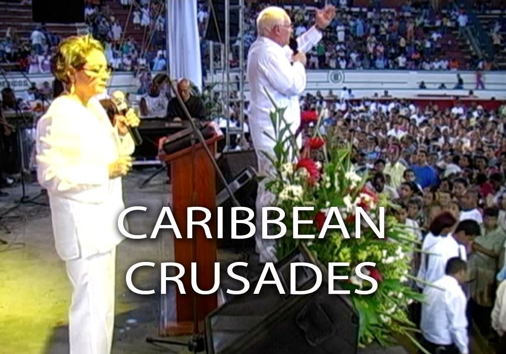 Man in white shirt preaching to large crowd; woman next to podium.