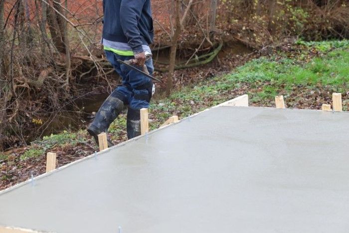 Person smoothing wet concrete on a form with wooden supports, outdoor setting.