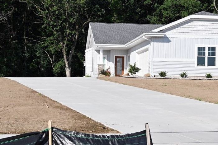 Driveway leading to a light blue house with a gray roof, surrounded by trees and newly seeded grass.