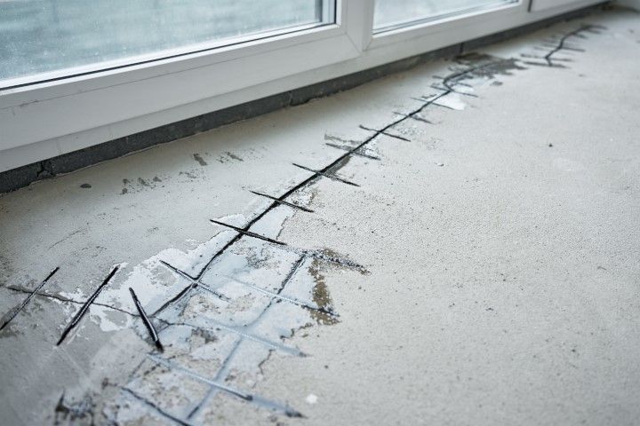 Concrete floor with exposed rebar along a crack, near a window. Gray concrete, white window frame.