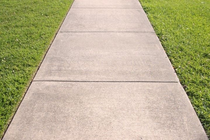 Concrete sidewalk flanked by green grass.