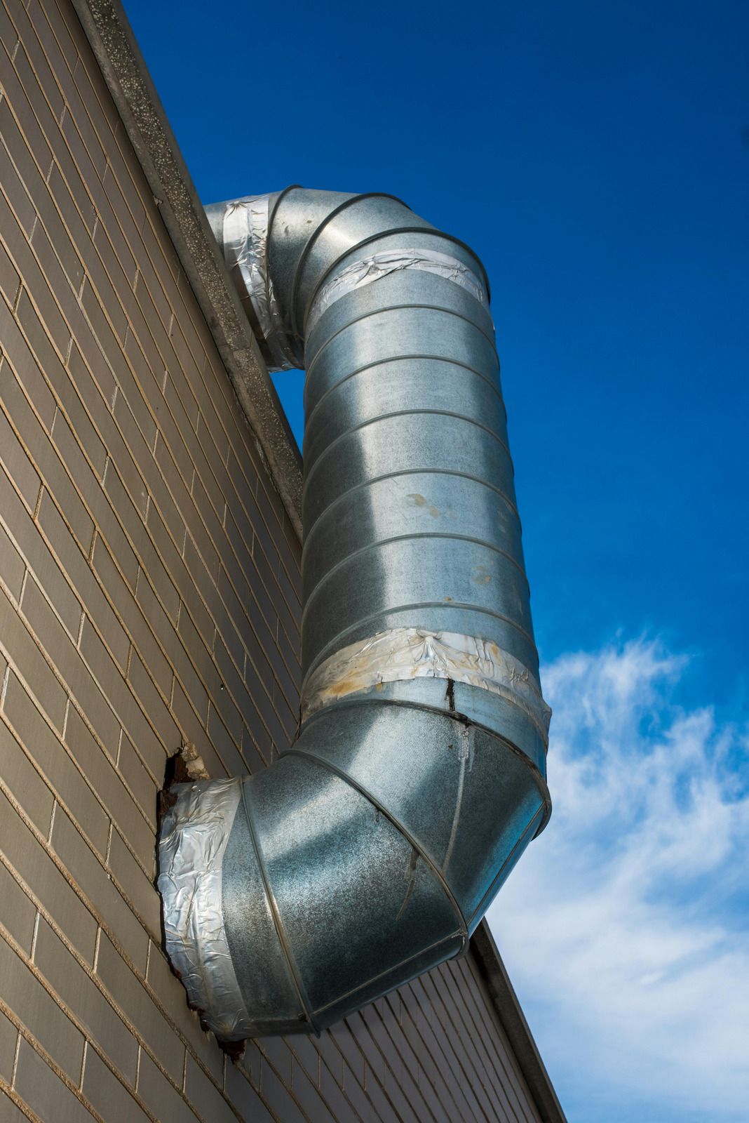 Metal ventilation pipe extending from a brick wall against a blue sky.