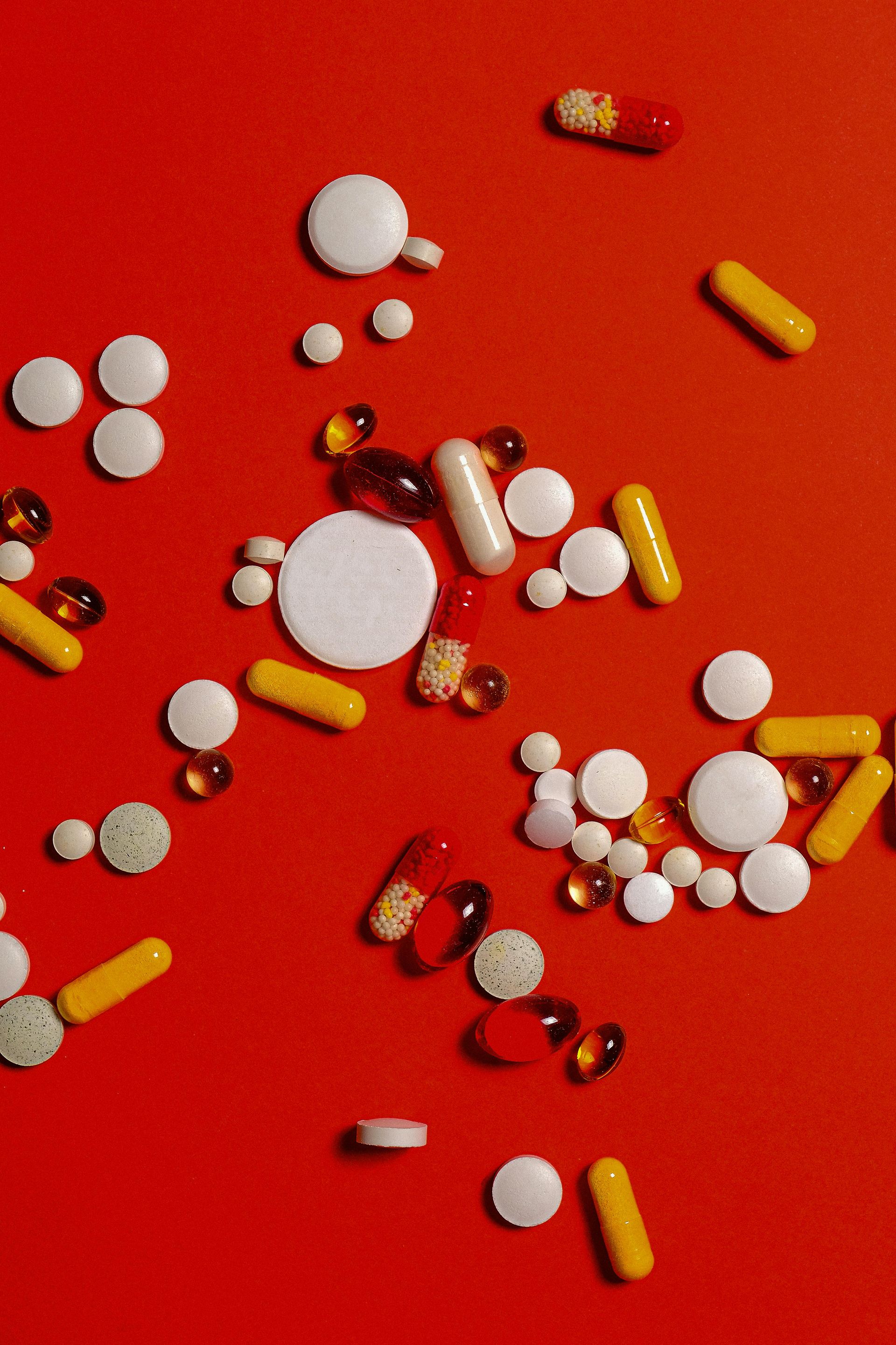 Many different types of pills are scattered on a red surface