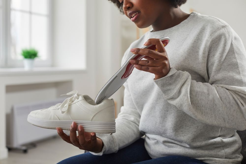 A woman is sitting on a couch holding a pair of white sneakers.