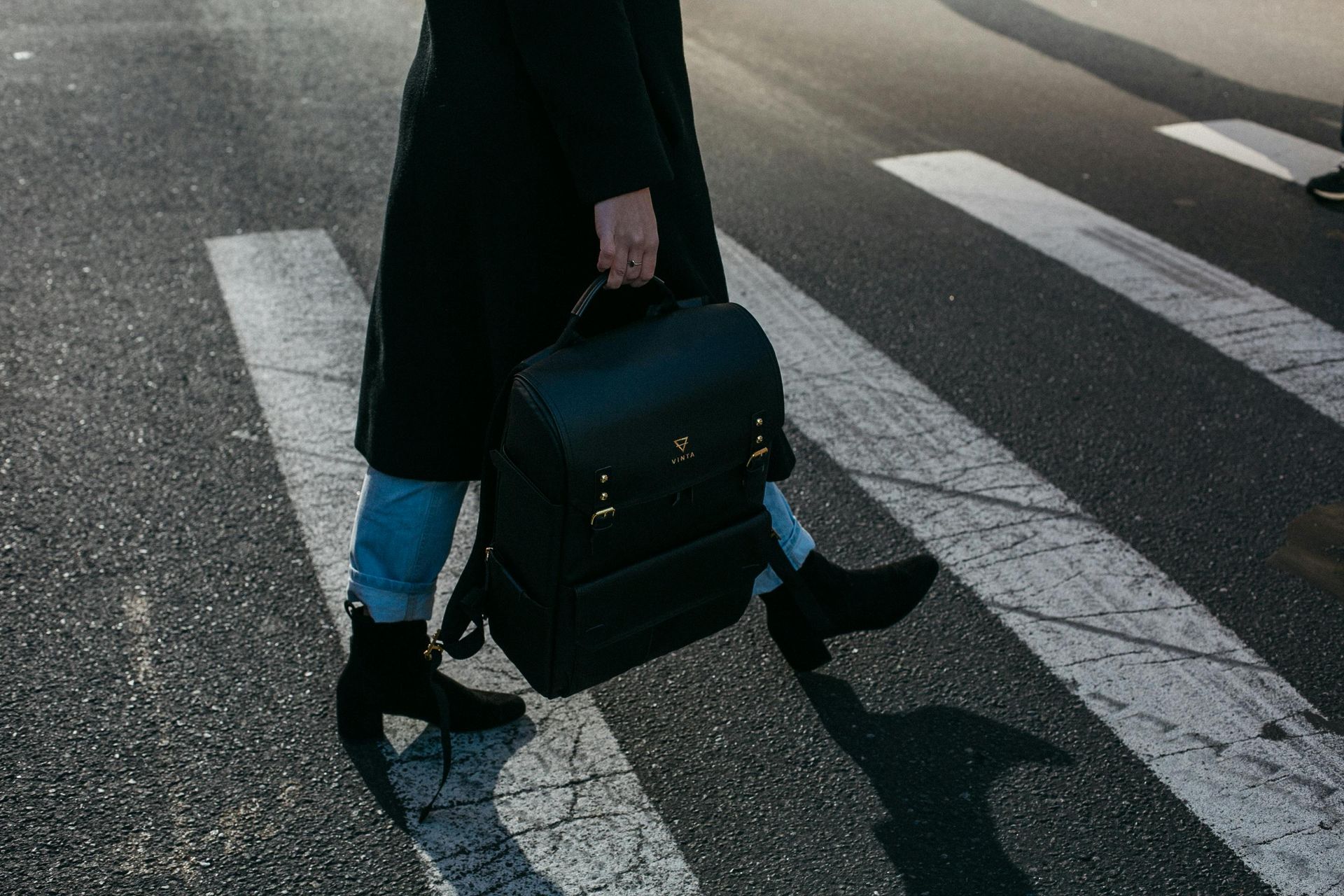 A woman is walking across a crosswalk while carrying a black briefcase.