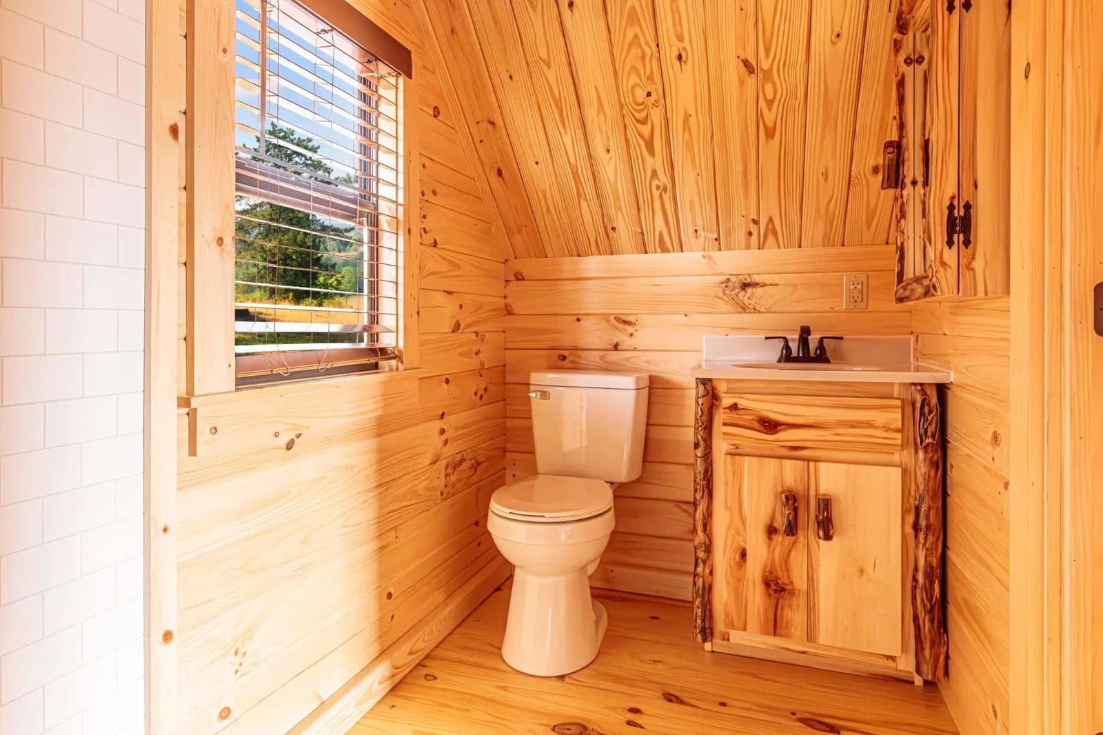 A bathroom in a log cabin with a toilet , sink and window.