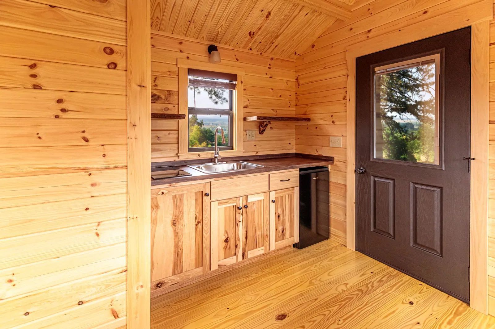 A kitchen in a log cabin with wooden cabinets and a black door.
