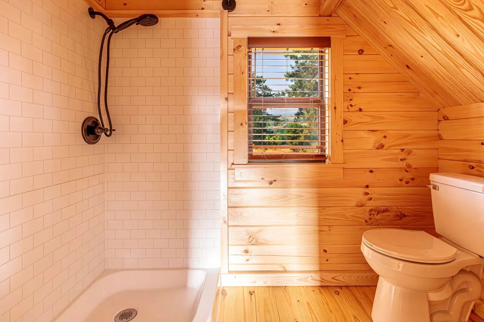 A bathroom in a cabin with a toilet , shower and window.