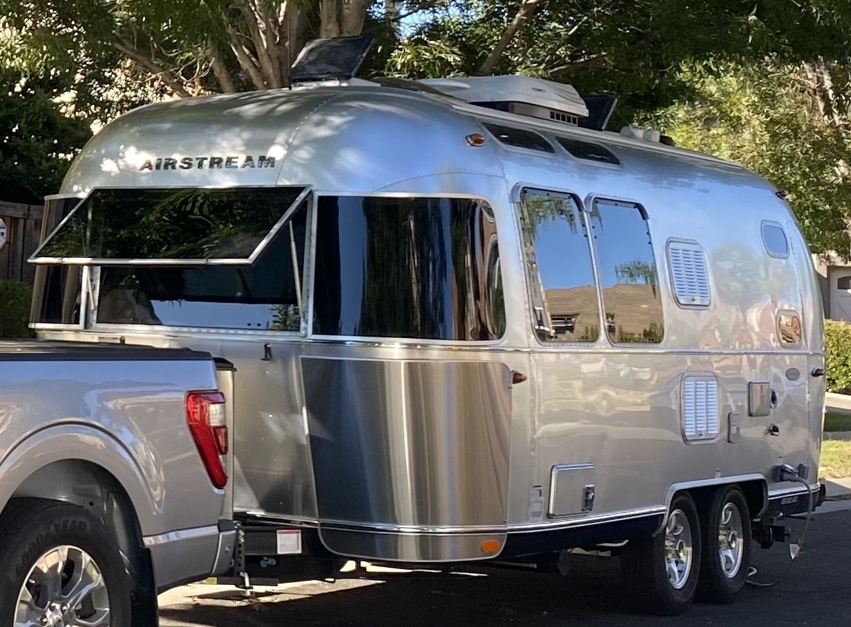 A silver airstream trailer is parked next to a truck.