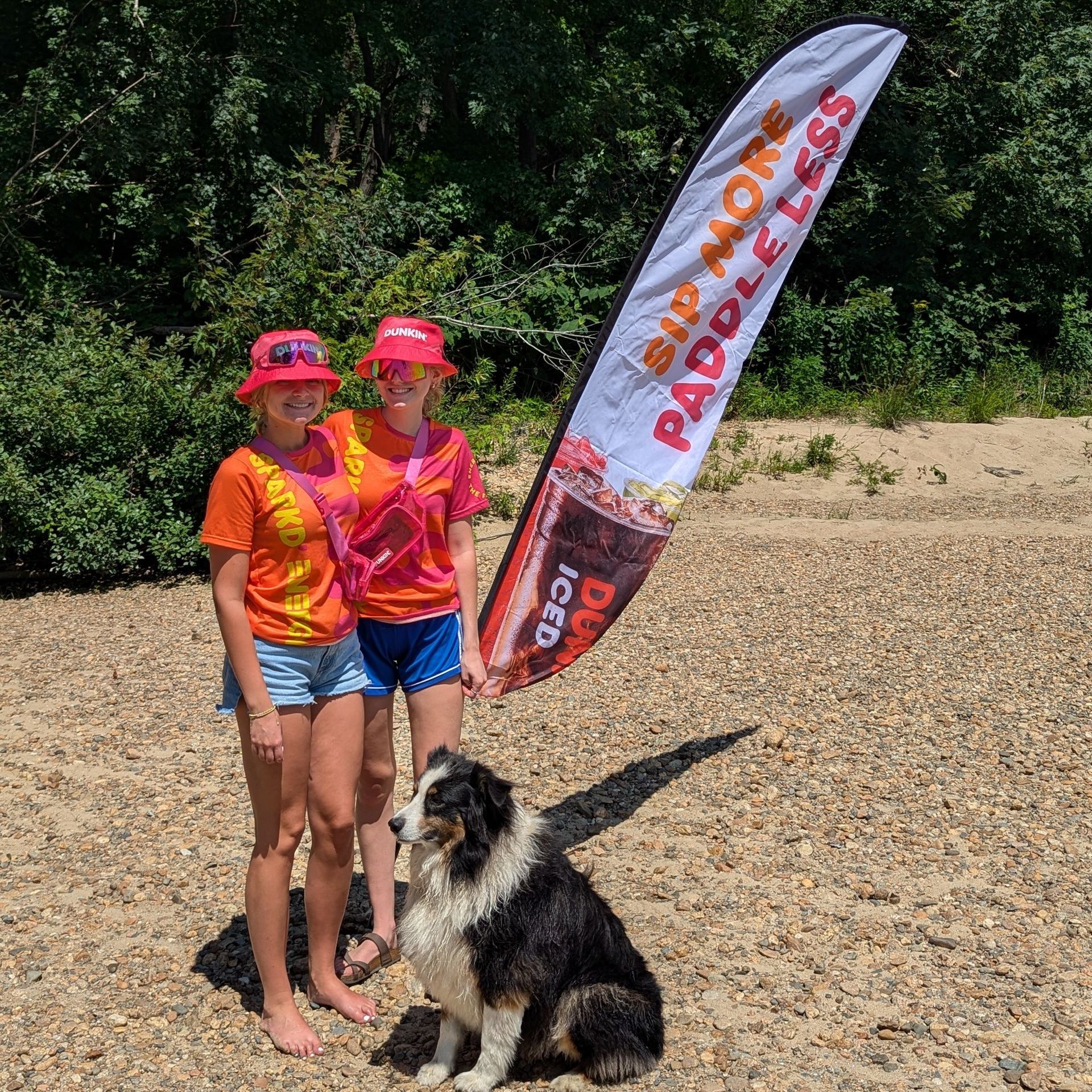 Two girls are standing next to a dog on a beach.