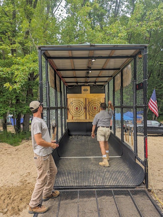 Two men are throwing axes at a target in a trailer.