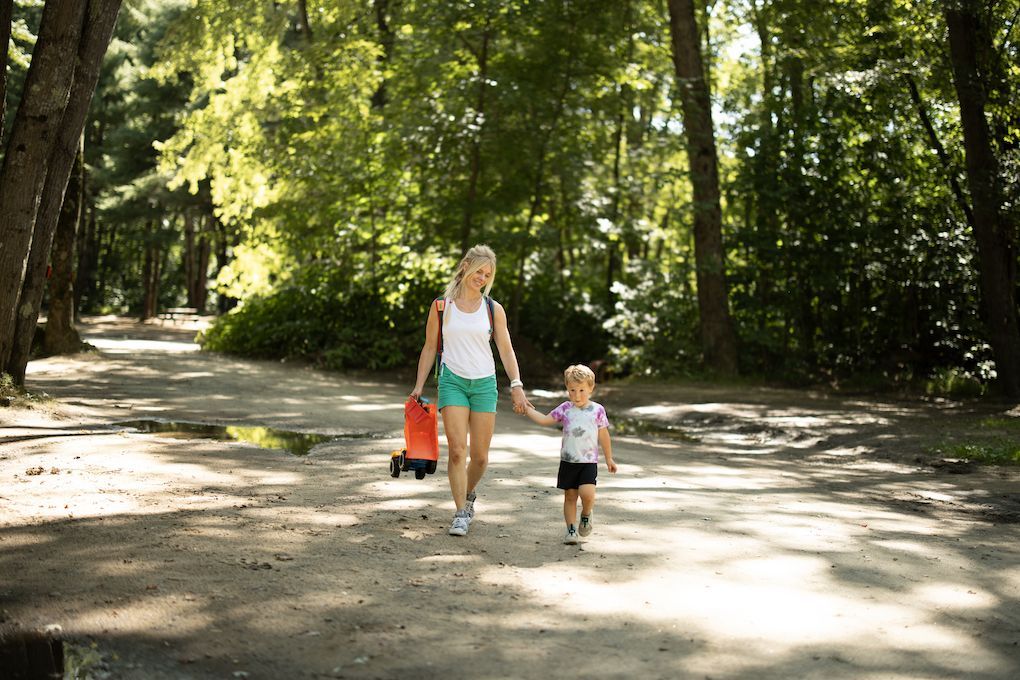 A woman and a child are walking down a path in the woods.