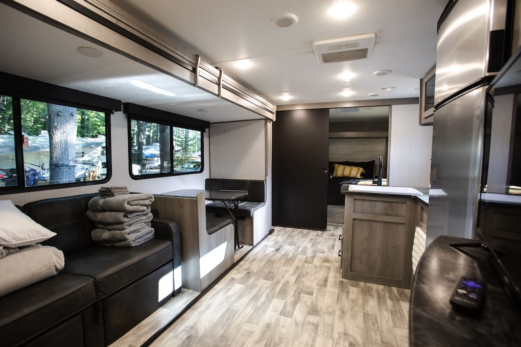 The inside of a rv with a couch , table , and refrigerator.