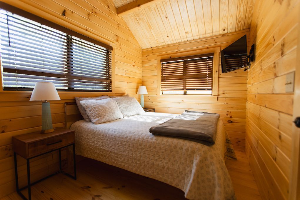 A bedroom in a log cabin with a bed , nightstand , lamp and television.