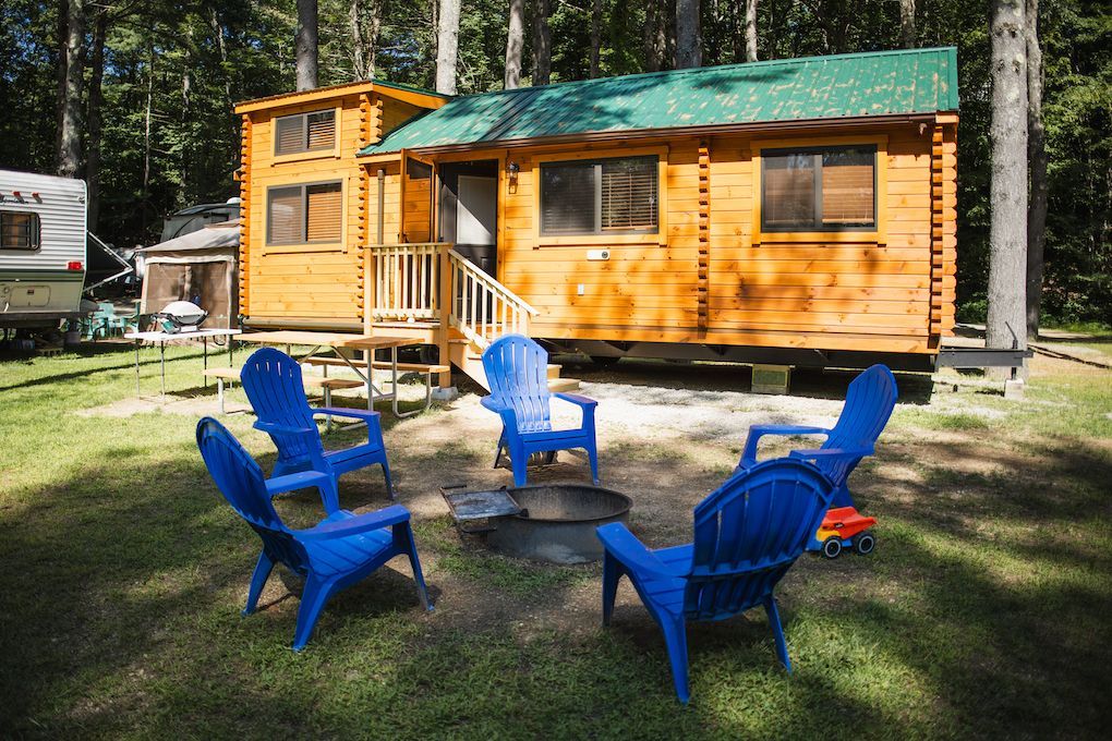 A group of blue chairs are sitting around a fire pit in front of a wooden cabin.