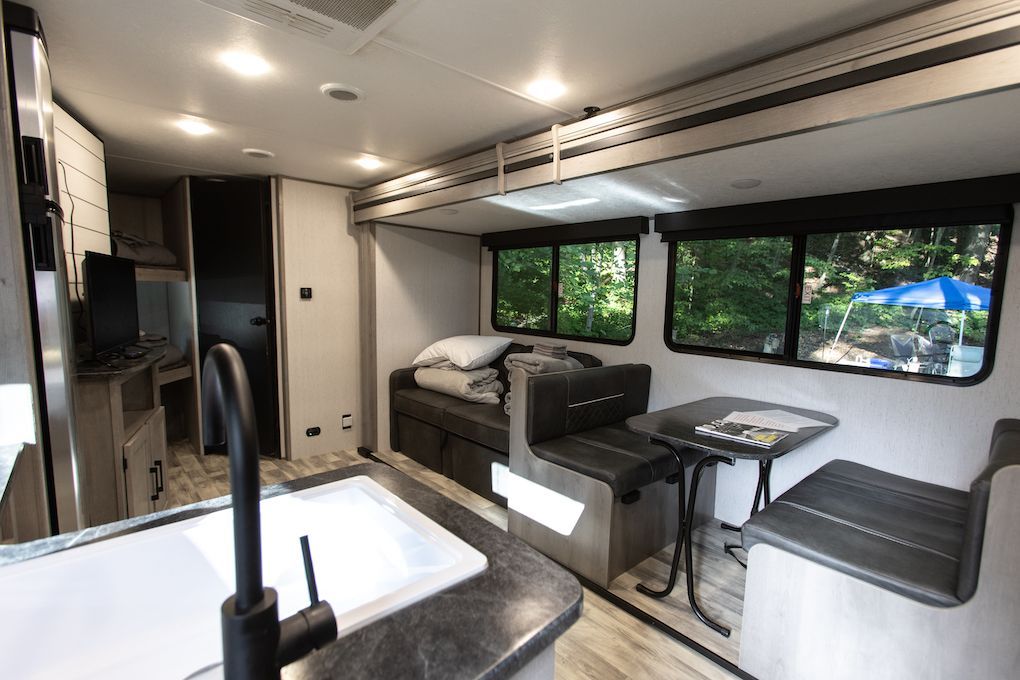 The inside of a rv with a sink , table and couch.