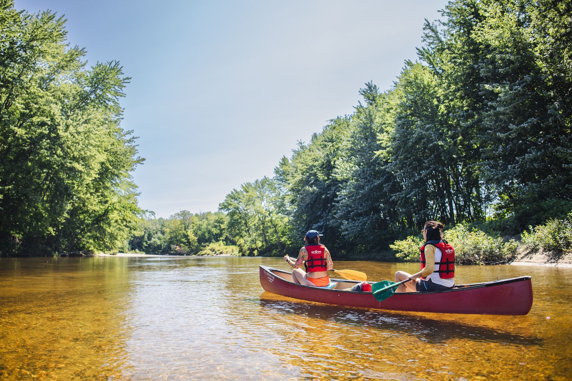 Two people are in a red canoe on a river.